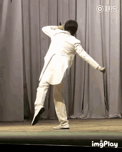a man in a white suit is dancing on a stage in front of a curtain with imgplay written on the bottom
