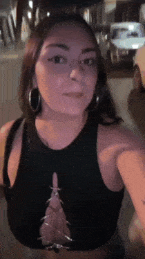 a woman wearing a black crop top and hoop earrings is taking a selfie