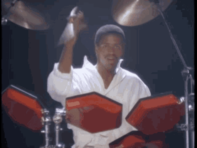 a man in a white shirt is playing drums with red pads that say yamaha on them