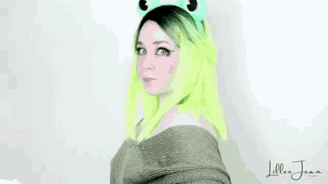 a woman with green hair and frog ears is wearing a sweater and a frog headband .