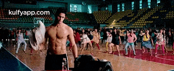 a man without a shirt is standing on a basketball court in front of a crowd of people .