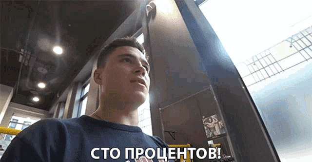 a man in a black shirt says " сто процентов " in front of a window