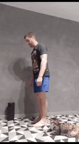 a man is standing on a checkered floor with a cat laying on the floor .