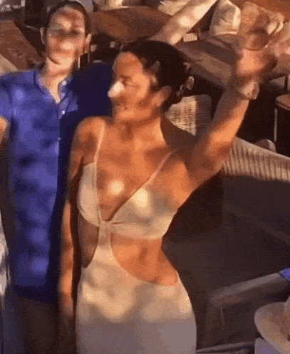 a woman in a white dress is standing next to a man in a blue shirt and waving .