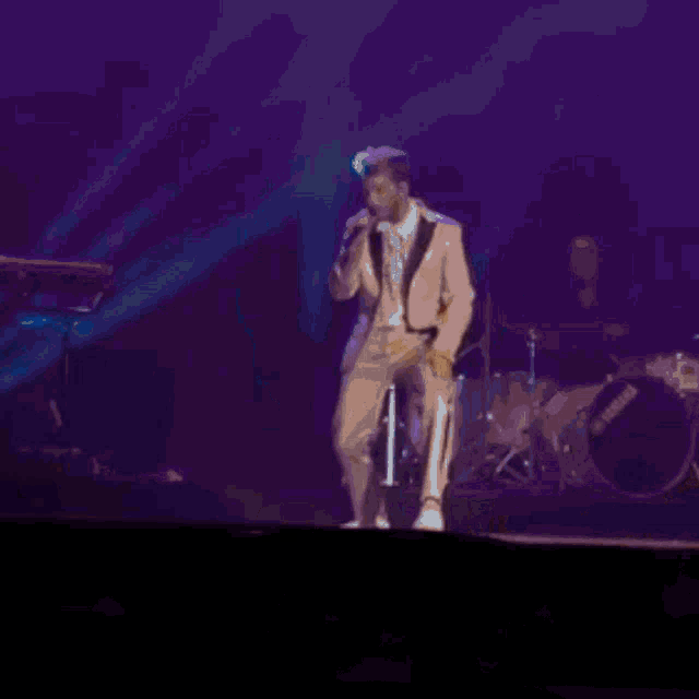 a man in a tan suit is singing into a microphone on a stage .