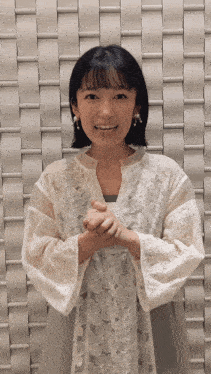 a woman wearing a white lace shirt is smiling in front of a white wall