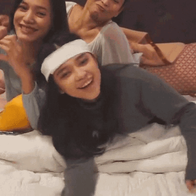 a woman wearing a headband is laying on a bed with other women