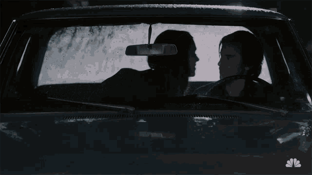 a man and a woman are sitting in a car with the nbc logo on the hood
