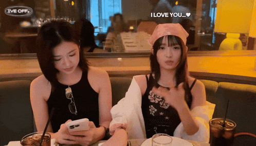two women are sitting at a table with a sign that says i love you on it