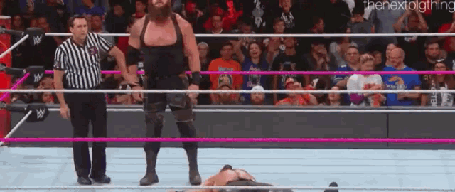 a wrestler is standing in the middle of a wrestling ring while a referee looks on .