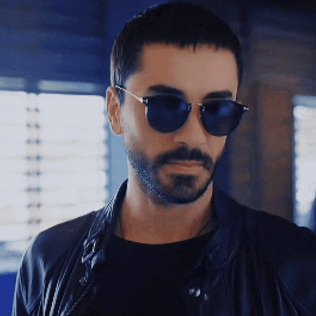 a man with a beard wears sunglasses and a black jacket