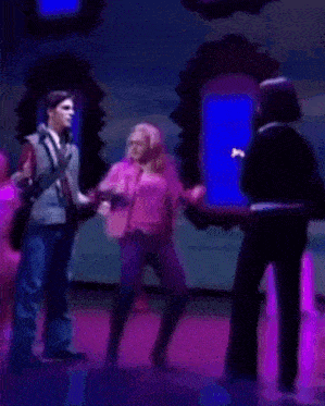 a group of people dancing on a stage with purple lights