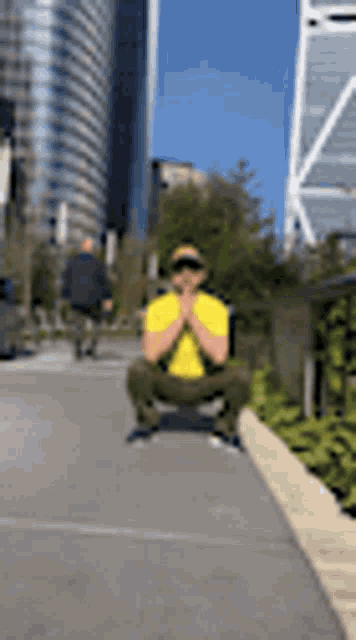 a man in a yellow shirt is squatting down on the sidewalk in front of a city skyline .