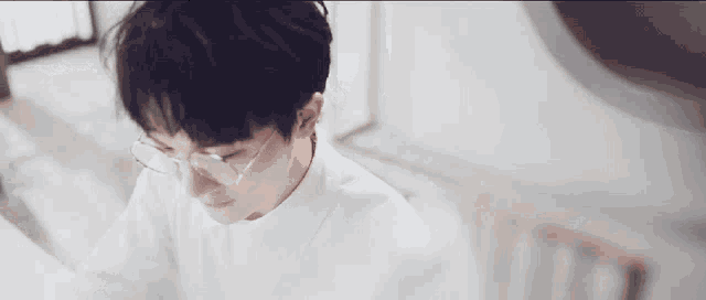 a young man wearing glasses and a white shirt is sitting at a table .