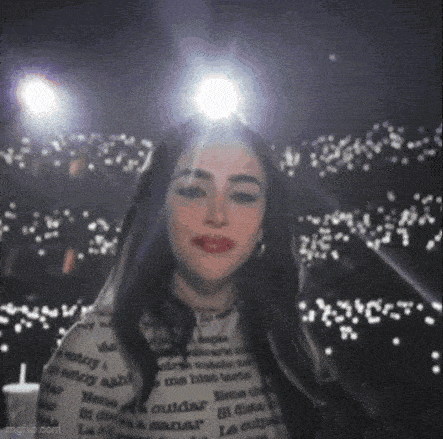 a woman with long black hair is standing in front of a crowd of people in a dark room .