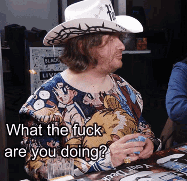 a man wearing a cowboy hat and a shirt that says what the fuck are you doing sits at a table