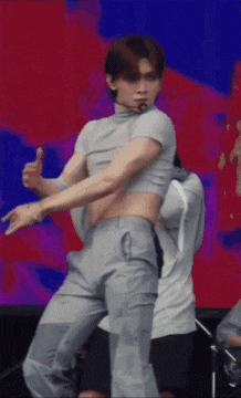 a man in a crop top and gray pants is dancing on a stage