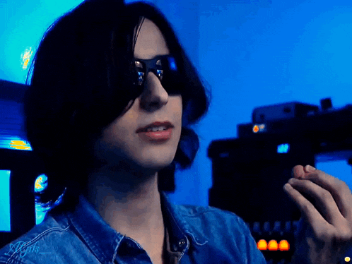 a man wearing sunglasses and a blue shirt is holding a small object in his hand .