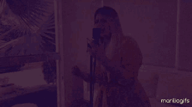 a woman in a yellow dress singing into a microphone with marilia.gifs written in the corner