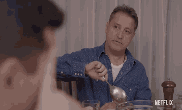 a man in a blue shirt sits at a table with a netflix logo in the background