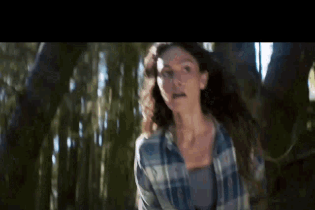 a woman in a plaid shirt is standing in the woods .