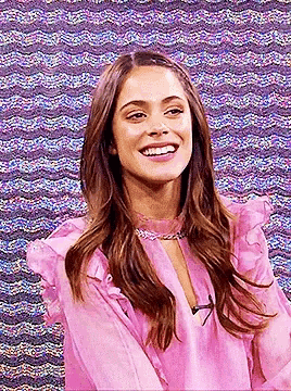 a woman in a pink blouse is smiling in front of a purple background .