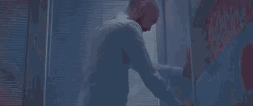 a man with a beard is standing in front of a window looking at his reflection in the mirror .