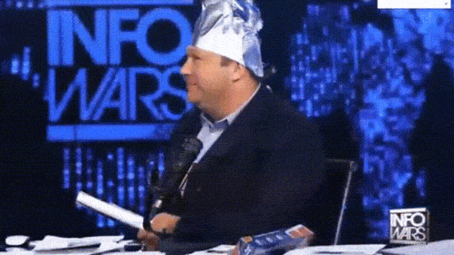 a man wearing a tin foil hat is sitting in front of a sign that says " info wars "