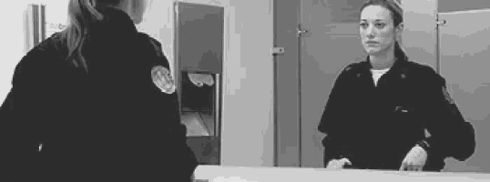 a woman in a police uniform is looking at her reflection in a bathroom mirror .