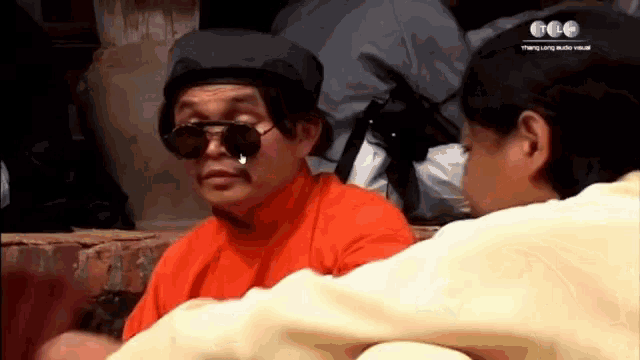 a man wearing sunglasses and a hat talks to another man