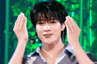a young man wearing a microphone and headphones is making a heart shape with his hands .