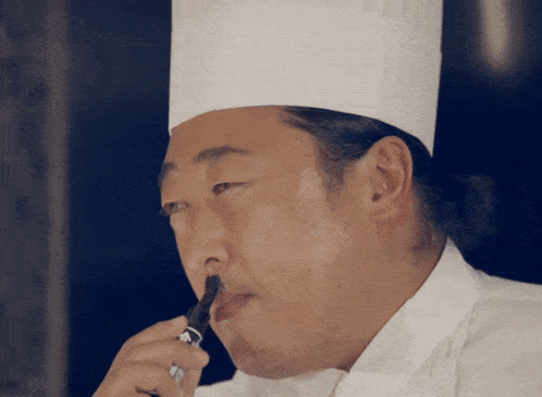 a man in a chef 's hat holds a marker in his mouth