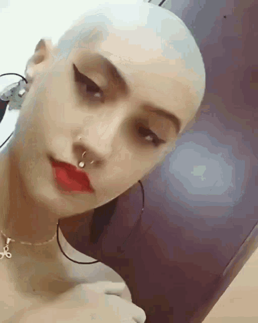 a woman with a nose ring and red lips has a shaved head