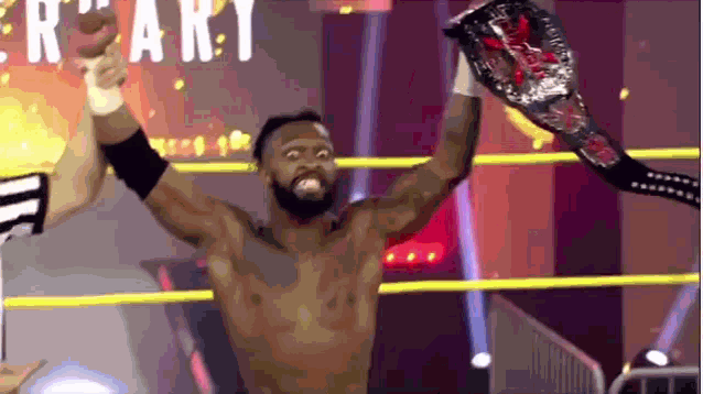 a man in a wrestling ring holds up his arms in the air