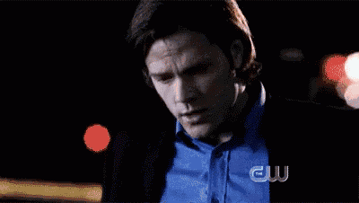 a man in a blue shirt is standing in front of a cw sign