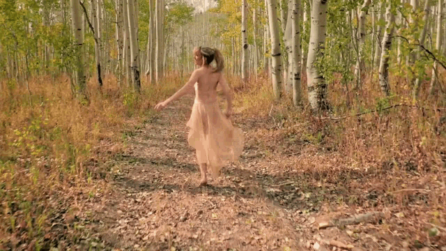 a woman in a white dress walking through a forest