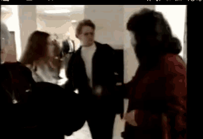 a man and two women are standing in a hallway talking to each other .