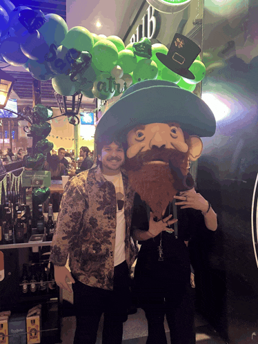 a man stands next to a leprechaun mascot in front of a sign that says ' irish '