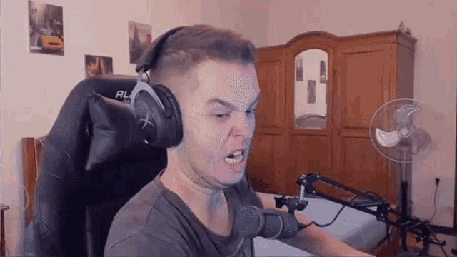 a man wearing headphones and a microphone is sitting in a chair in a bedroom .