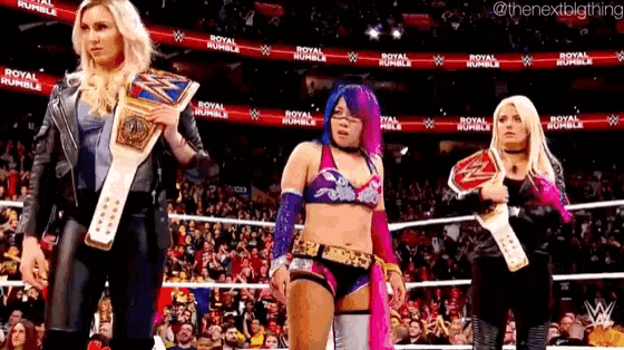 a group of female wrestlers are standing in a ring holding championship belts .