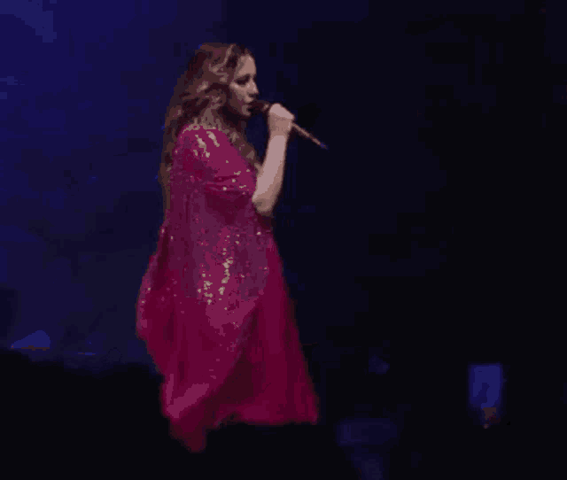 a woman is singing into a microphone while wearing a pink dress .