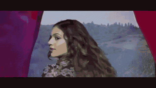 a woman with long hair is standing in front of a red curtain