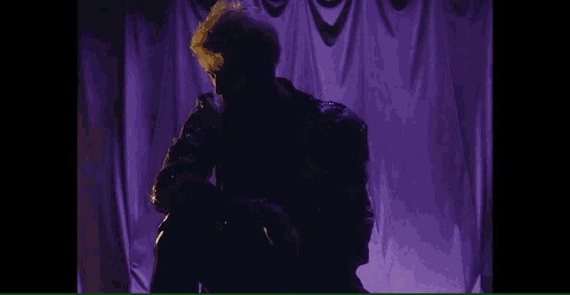 a silhouette of a man sitting in front of a purple curtain