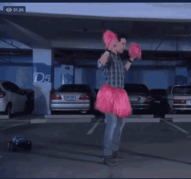 a man in a pink dress is standing in a parking garage with cars and a sign that says d5