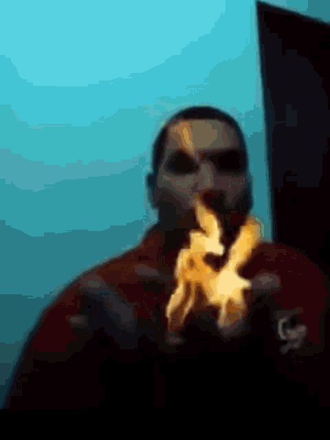 a man is blowing flames out of his mouth while wearing a red shirt .