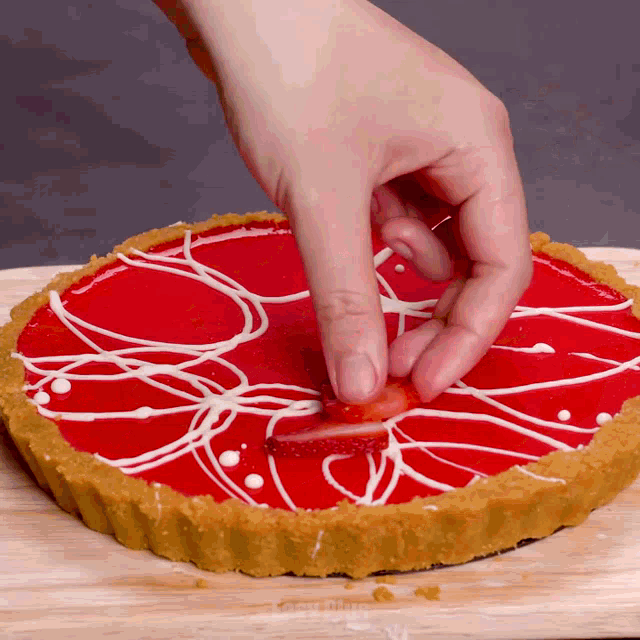 a person is adding a slice of strawberry to a red pie