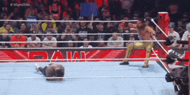 a wrestler is kneeling down in the middle of a wrestling ring while a crowd watches .