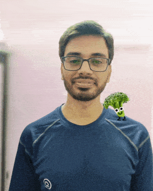 a man wearing glasses and a blue shirt has a picture of a broccoli on his shoulder