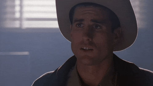 a man wearing a cowboy hat looks at the camera with a serious look on his face