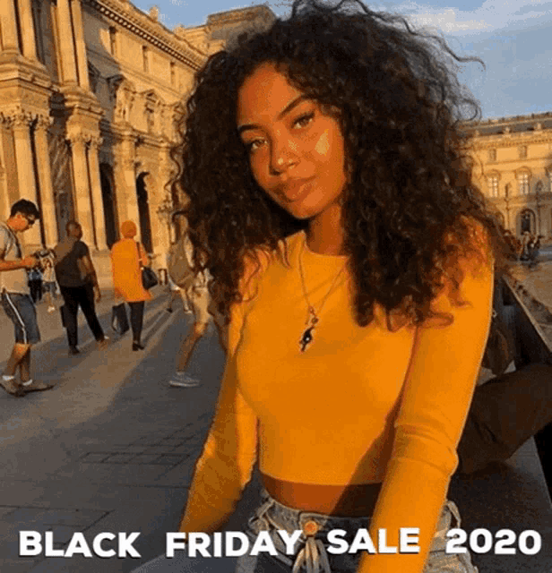 a woman with curly hair is wearing a yellow top and jeans